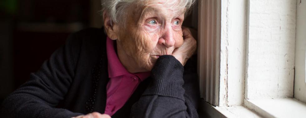 Ältere Frau schaut aus dem Fenster, sitzend, nachdenklich, Tageslicht erhellt den Raum.