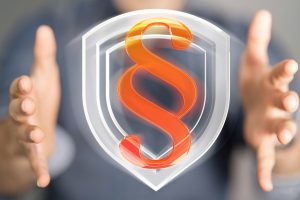 Ein rotes Paragrafenzeichen schwebt zwischen Händen vor einem transparenten Schutzschild.